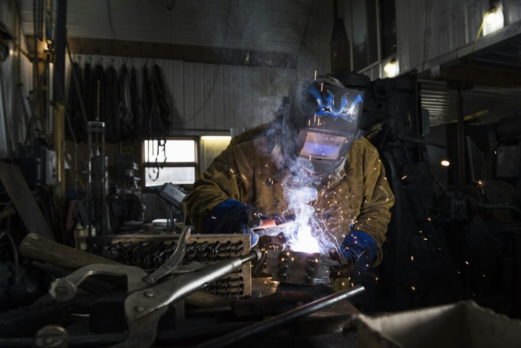 Blacksmith in welding mask welding metal in workshop